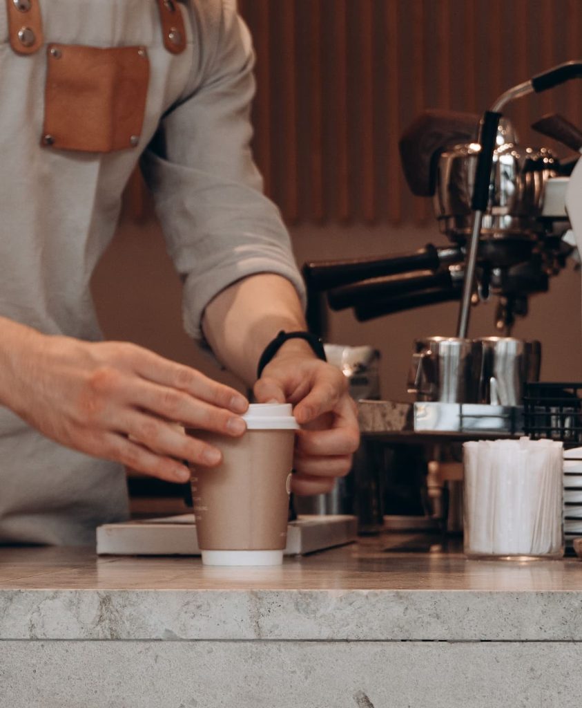 Barista τοποθετεί καπάκι σε χάρτινο ποτήρι καφέ στον πάγκο take away cafe